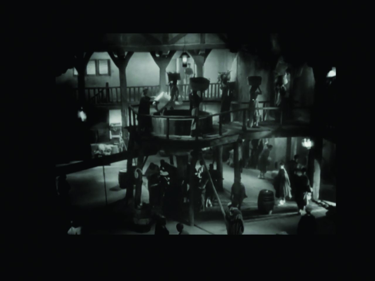 A lightly blurry black and white film still of workers standing beneath and on top of a balcony.