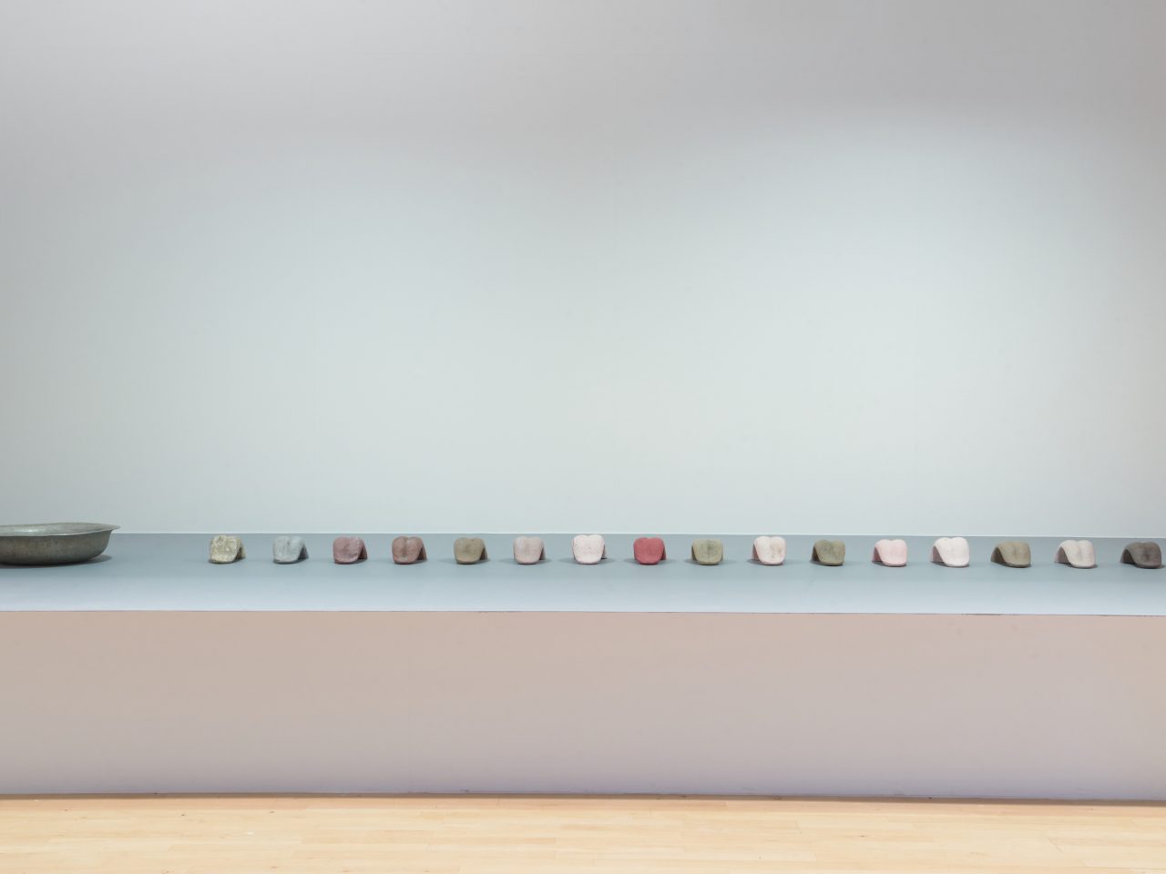 An installation of ceramic tounges, painted in white, green and red. There is a steel bowl to the left of the row of tounges.