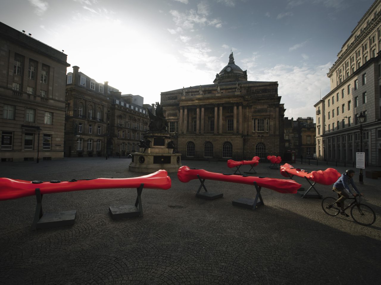 A installation within Exchange Flags, there are multiple large bone shaped canoes, they are bright red and are sat on metal stands.