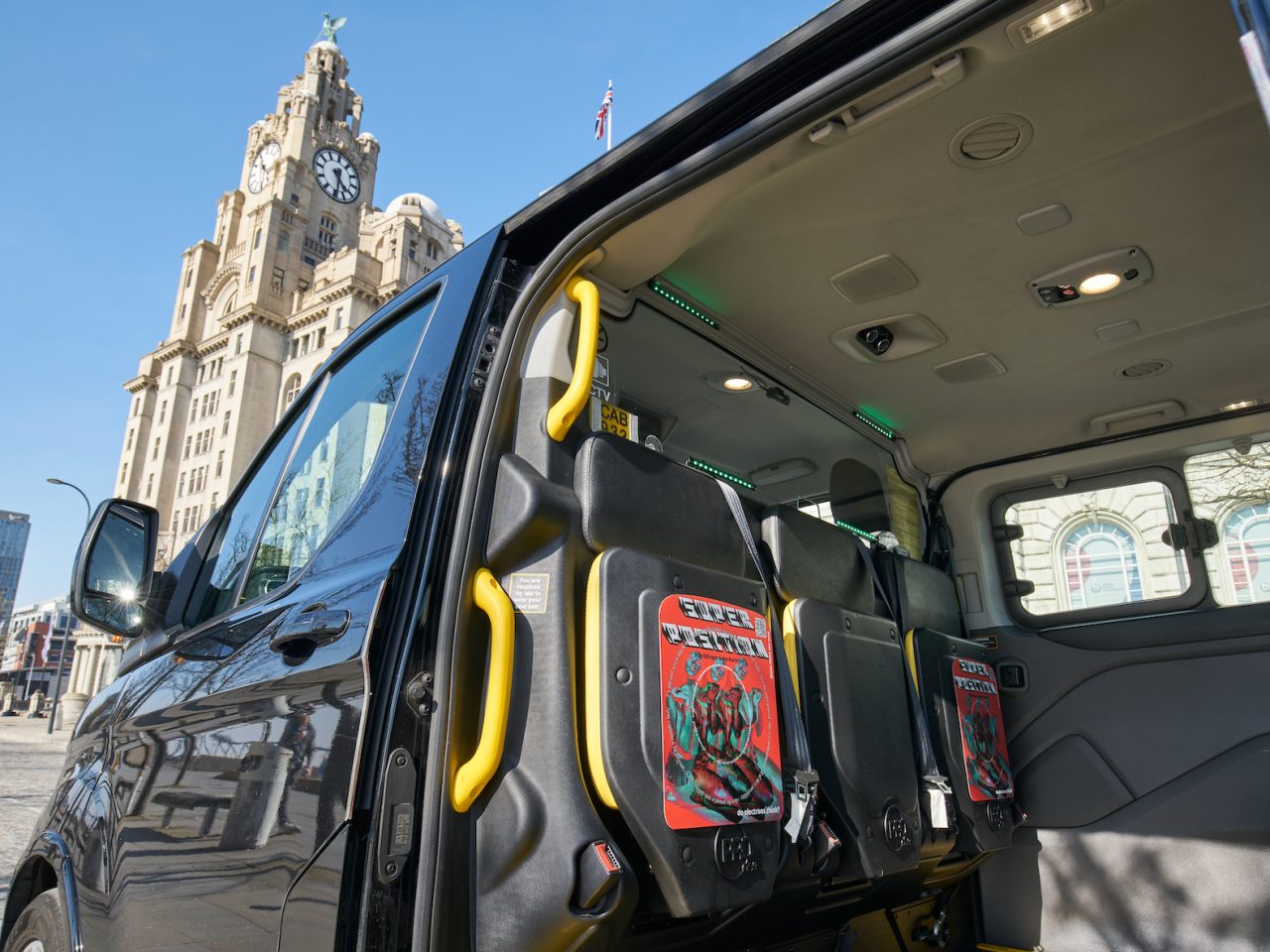 a shot inside a black cab with two of the same plaque on the back of the chairs. In the background you can see the liver building.