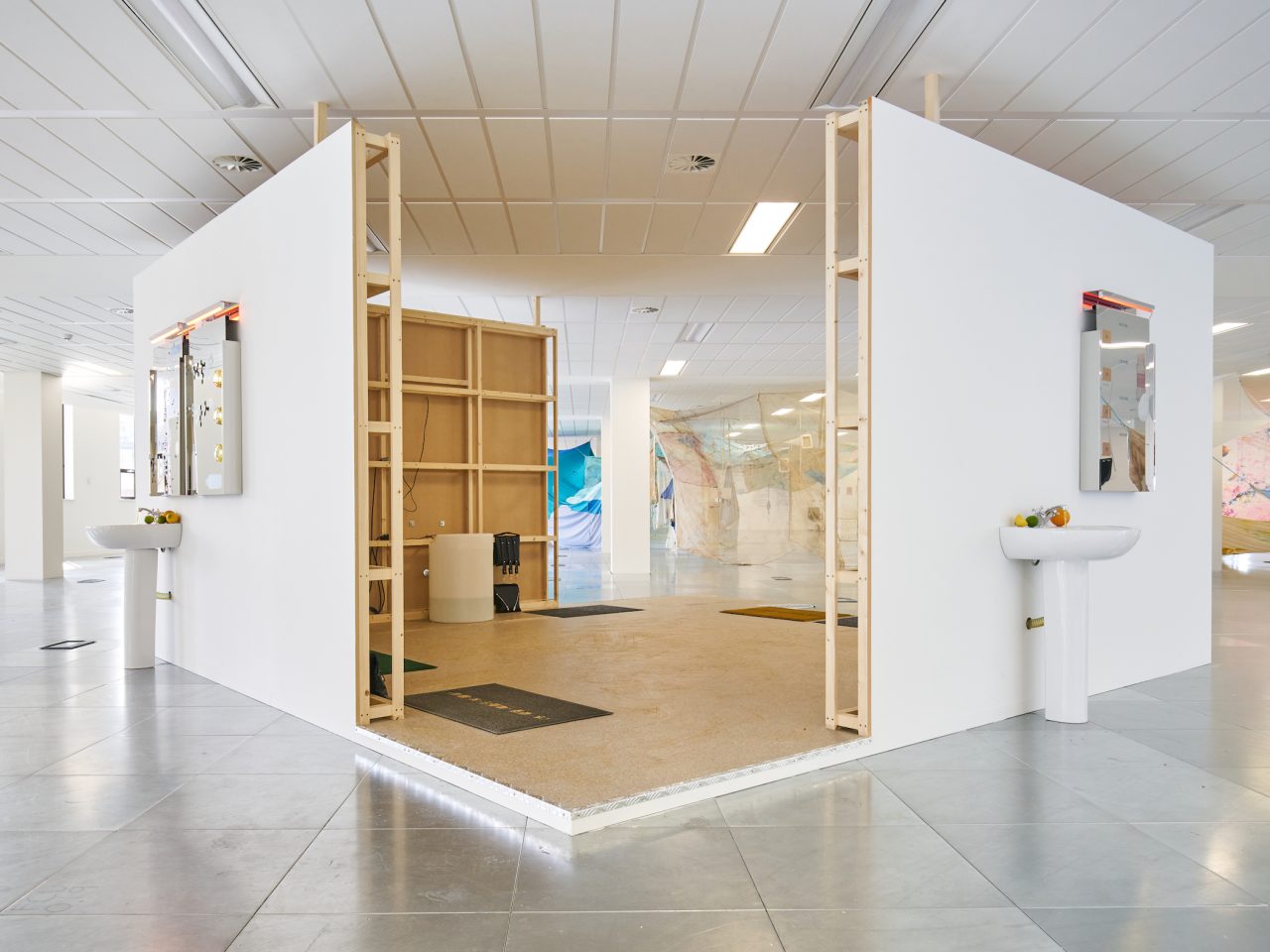 A wooden build structure. On the outside of the cubed structure are two sinks filled with fruit and bathroom mirrors hung above them.