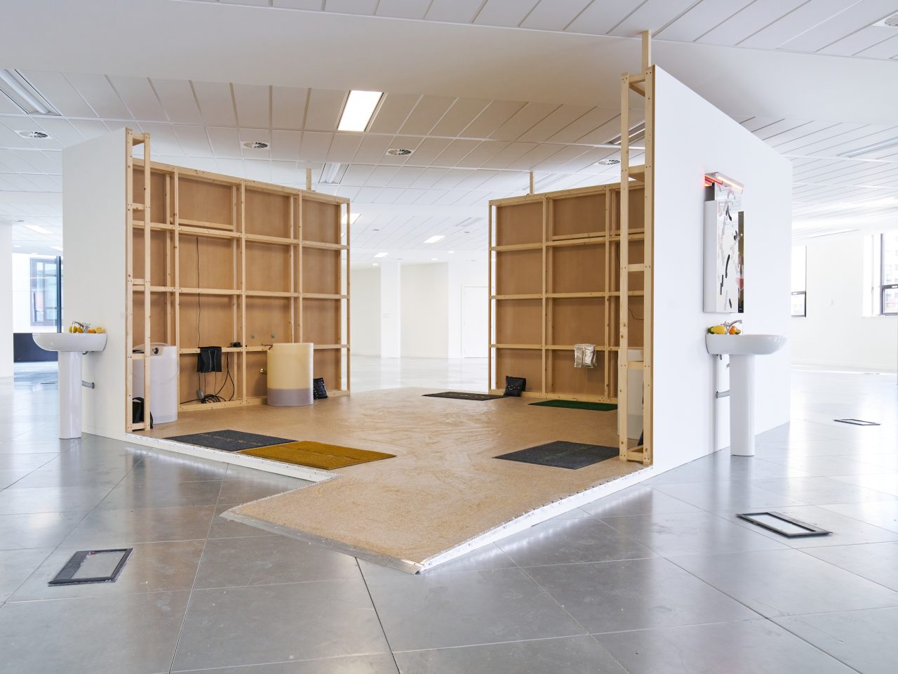 A wooden build structure. On the outside of the cubed structure are two sinks filled with fruit and bathroom mirrors hung above them.