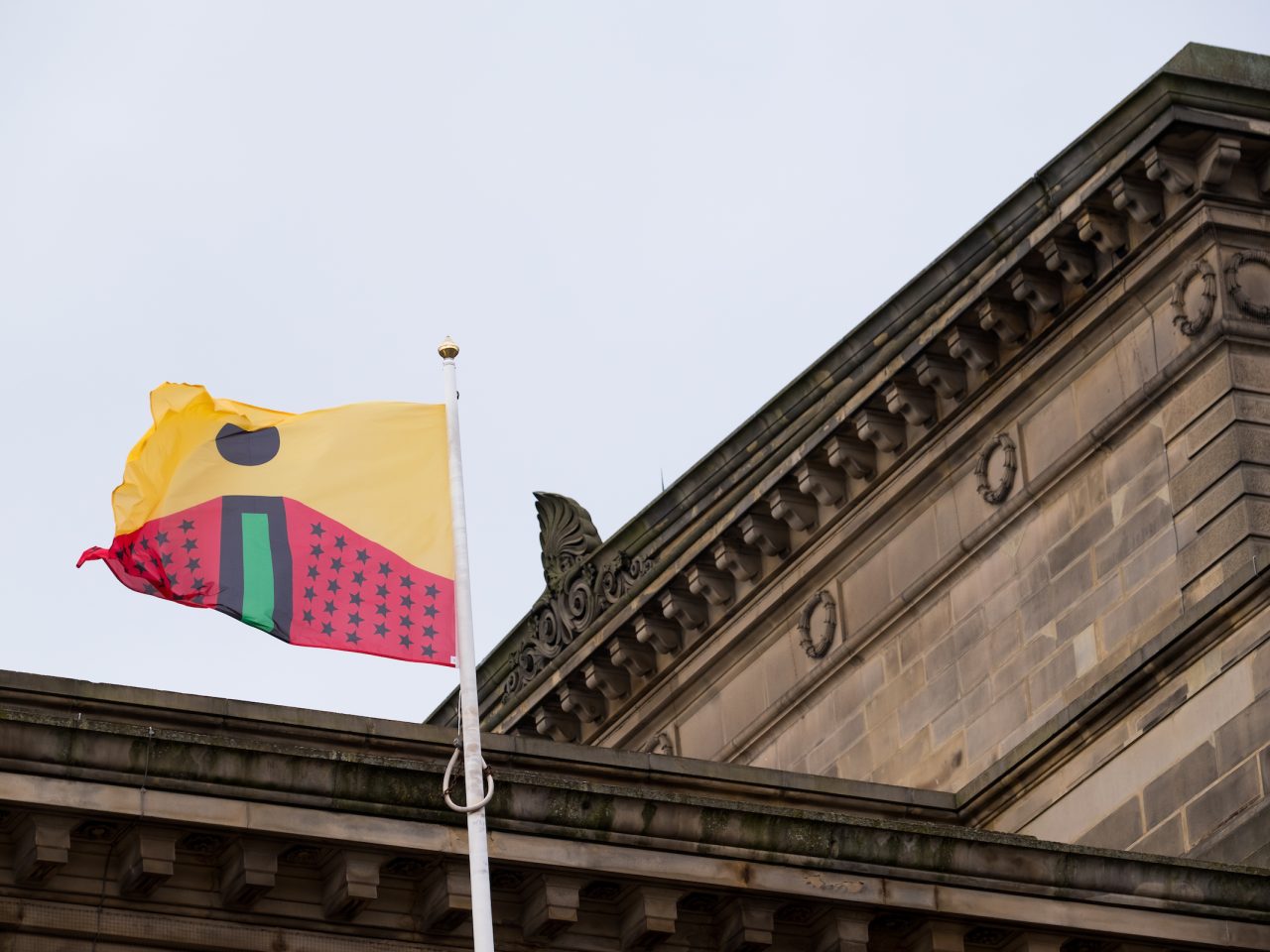 A flag designed by the artist, designed based on the colours of the african flag. The top half of the flag is yellow with a black circle and the lower half is red with lots of black stars and a green line in the centre.