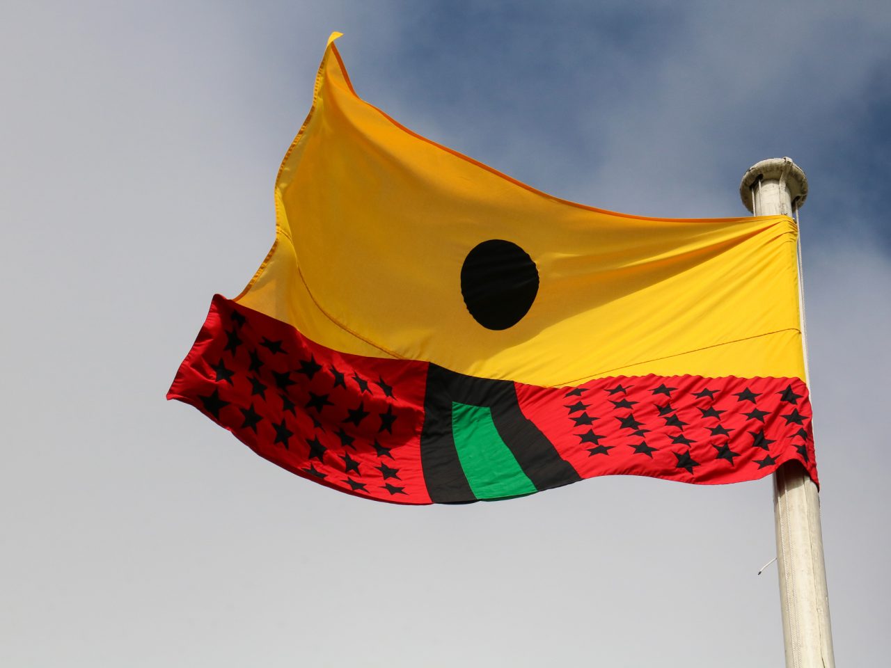 A flag designed by the artist, designed based on the colours of the African flag. The top half of the flag is yellow with a black circle and the lower half is red with lots of black stars and a green line in the centre.