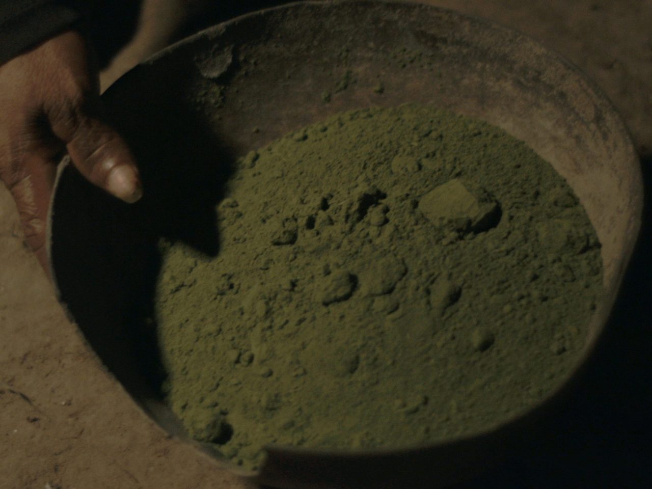 A film still of someone holding a steel bowl of dirt.