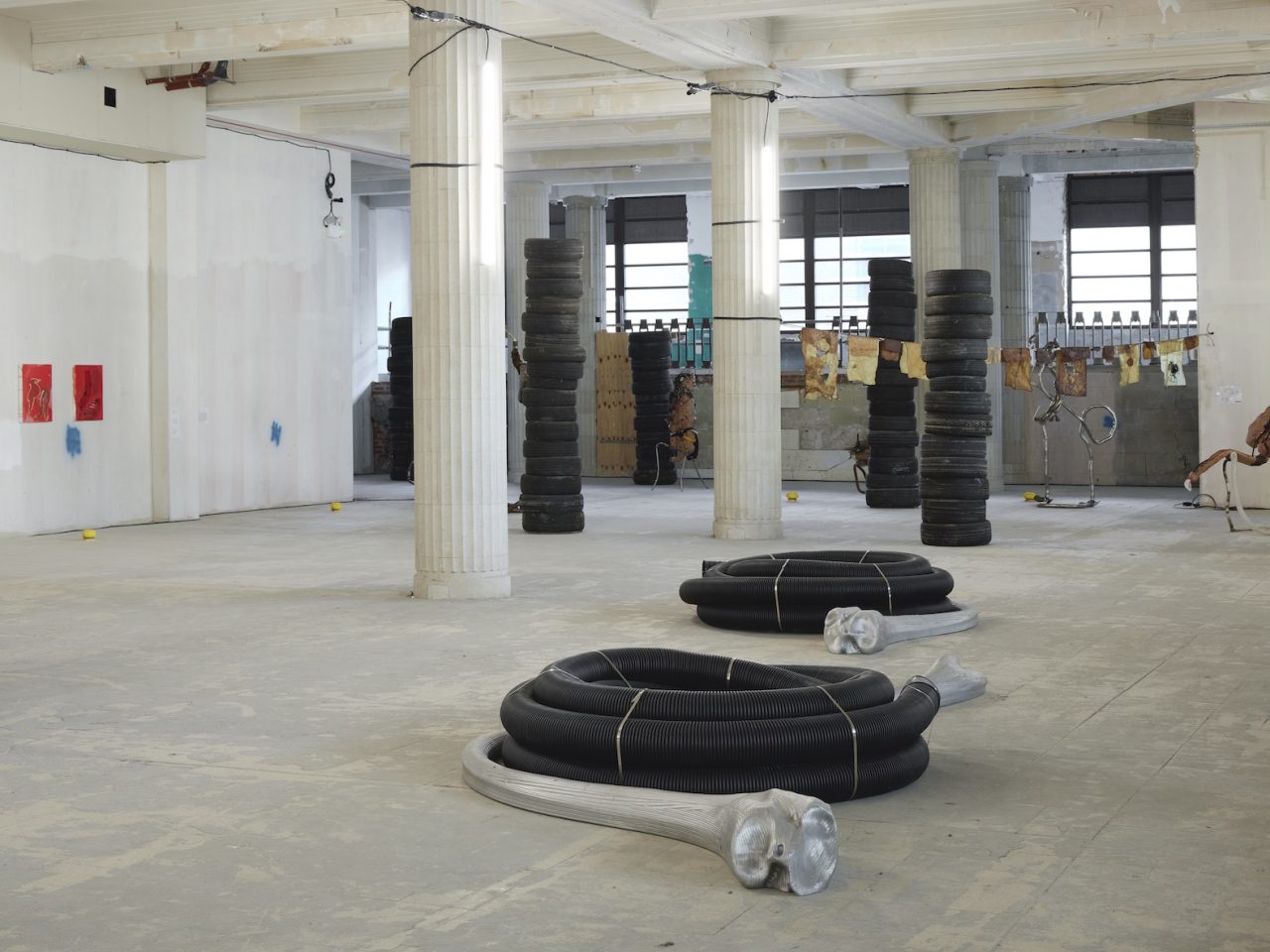 Large floor sculptures, they are long black tubes tied together to create a circular structure, underneath them is a large-scale stretched aluminium model of a human bone curving outwards.