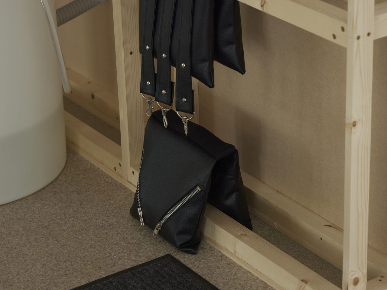 Two leather artworks, one with with two silver zips on the front and another hanging above with 3 leather bag handles dangling on the front.