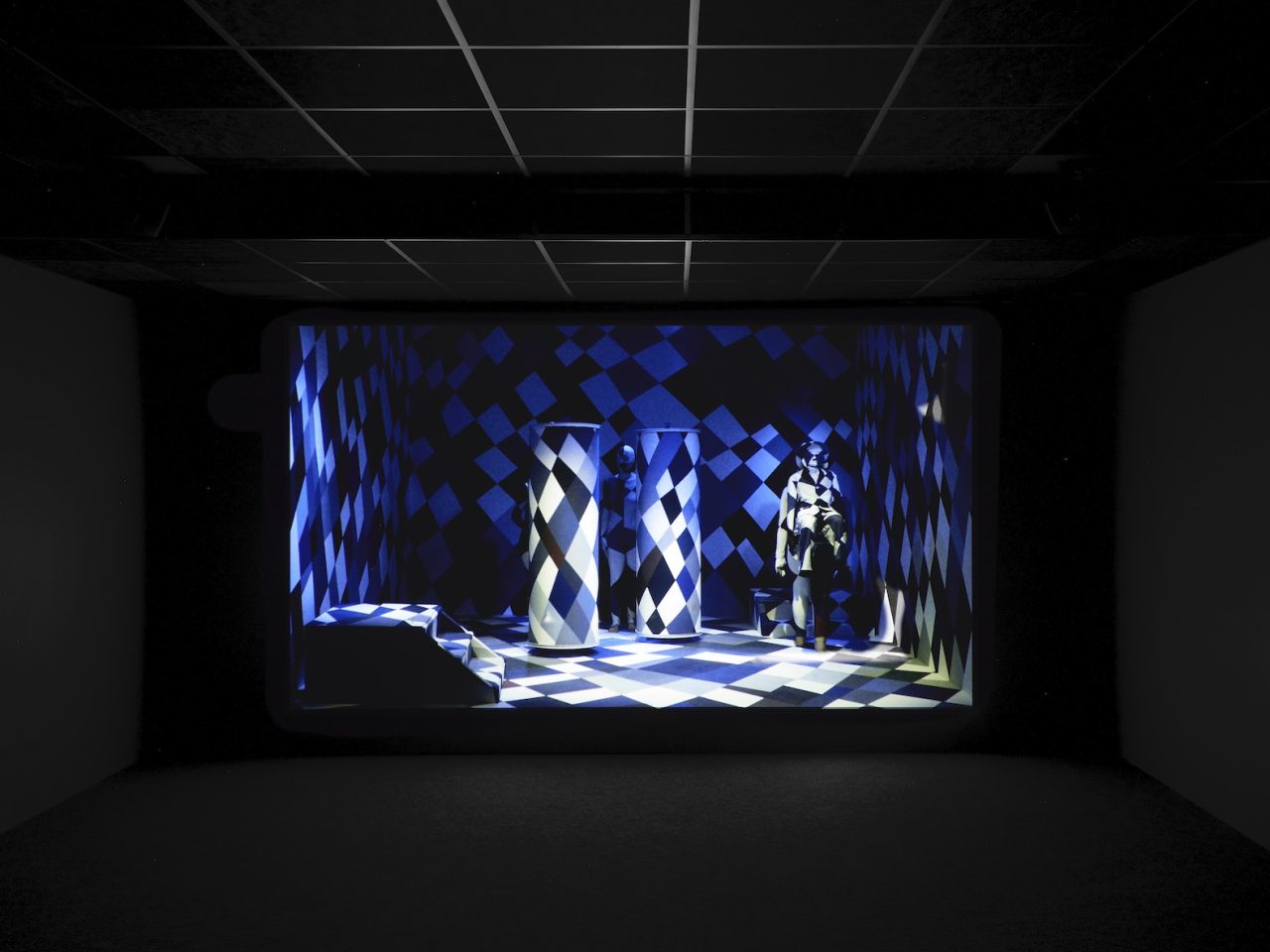 Two pillars, steps and a person in a boxed room. The people, objects and room they are in are all camouflaged together in a blue and white checkered pattern.