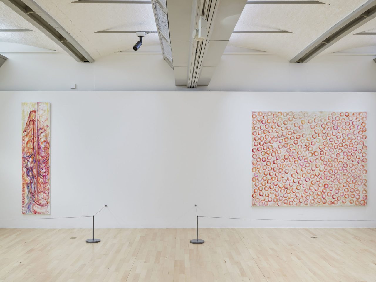 One large painting with pink and orange circles covering the canvas and a long vertical painting with orange, pink and purple abstract markings.