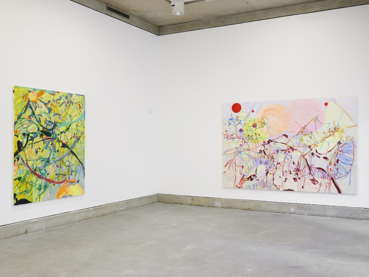 Two large abstract paintings on a white wall, the painting on the left is mostly yellow with blue markings and the painting on the right is mainly light pink with yellow, red and blue markings.