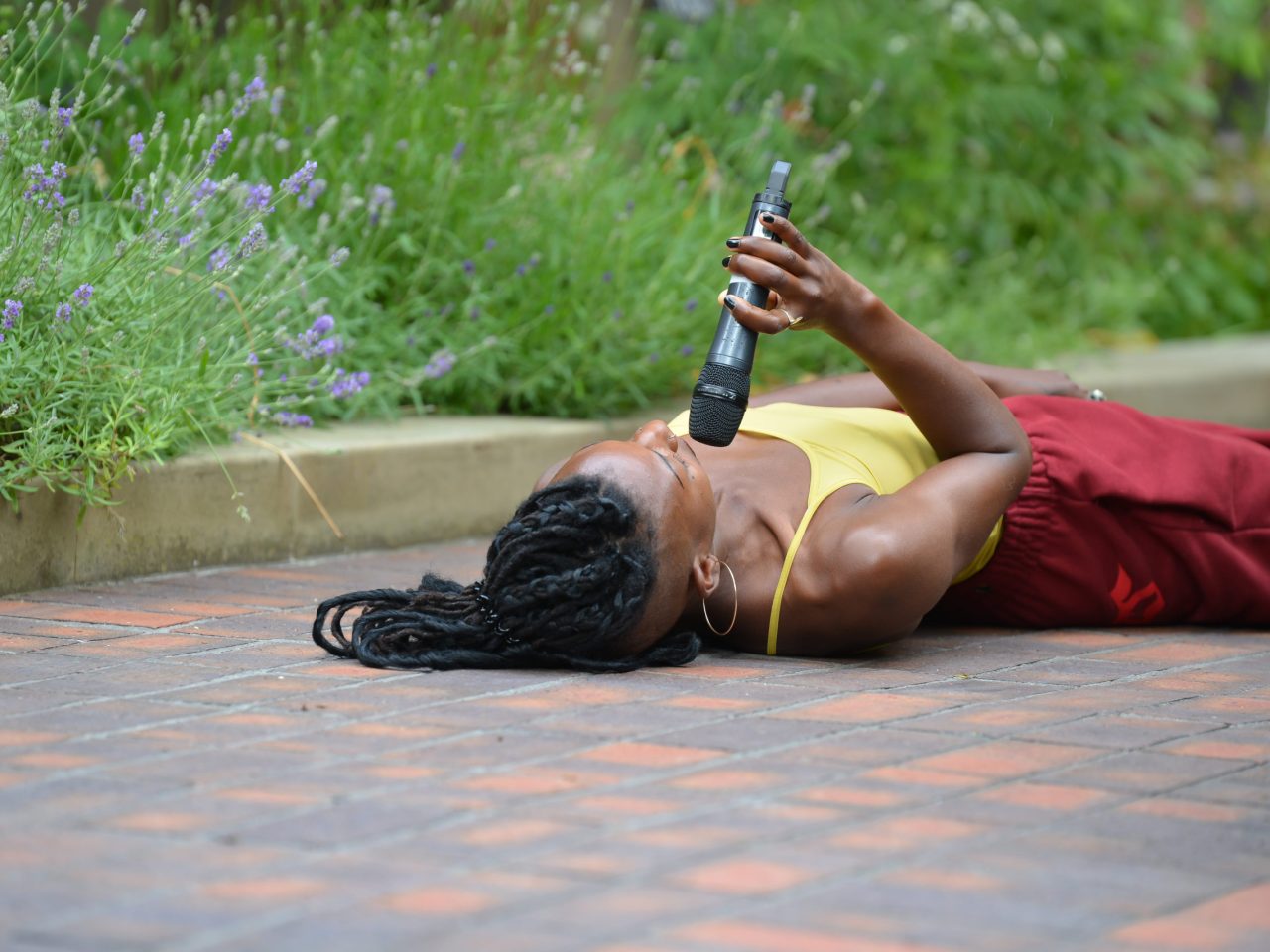 The artist lying on the ground face up, holding a microphone to their face.