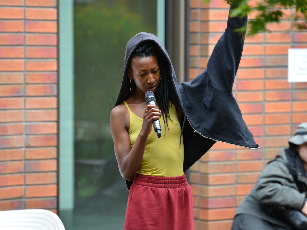 The artist speaking into a mic with one hand up.