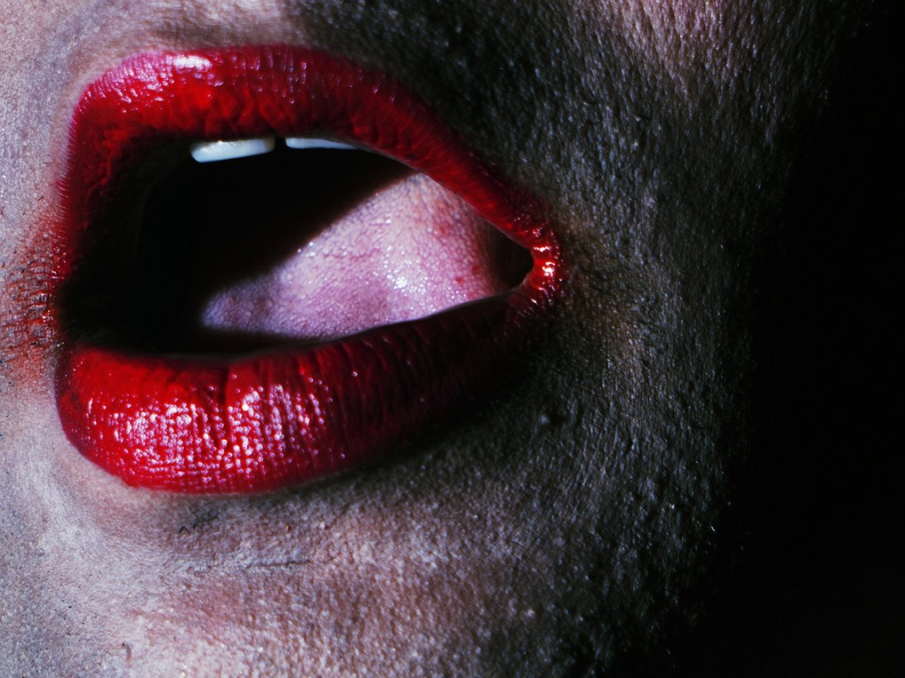 A close up of someones mouth open with bright red lipstick on.