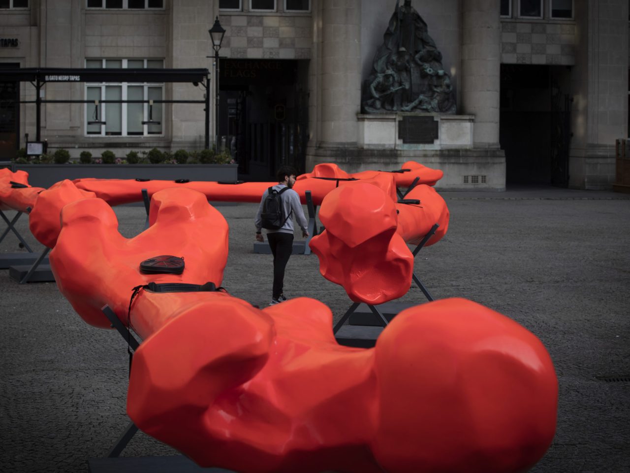 A installation within Exchange Flags, there are multiple large bone shaped canoes, they are bright red and are sat on metal stands.