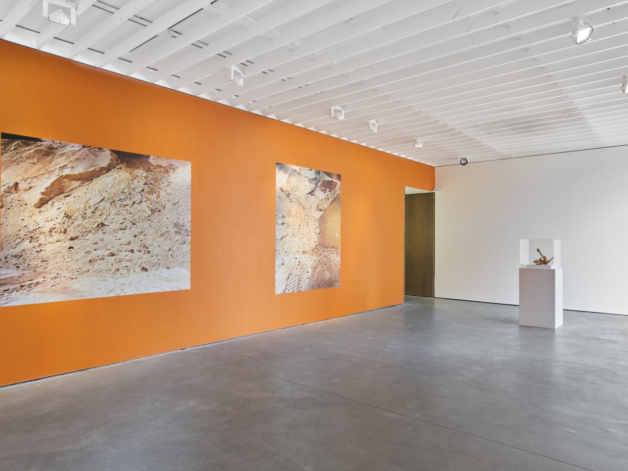 Two large vinyl stickers on a orange wall at Open Eye Gallery. The vinyl are photographs of the inside of a sugar factory. There is a white plinth with a sculpture in the shape of an anchor.