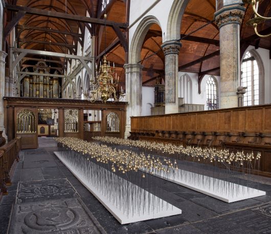 An installation of 2 long pathways of bells. It has a walkway in the middle so you can walk through it, this installation is inside a church⁠