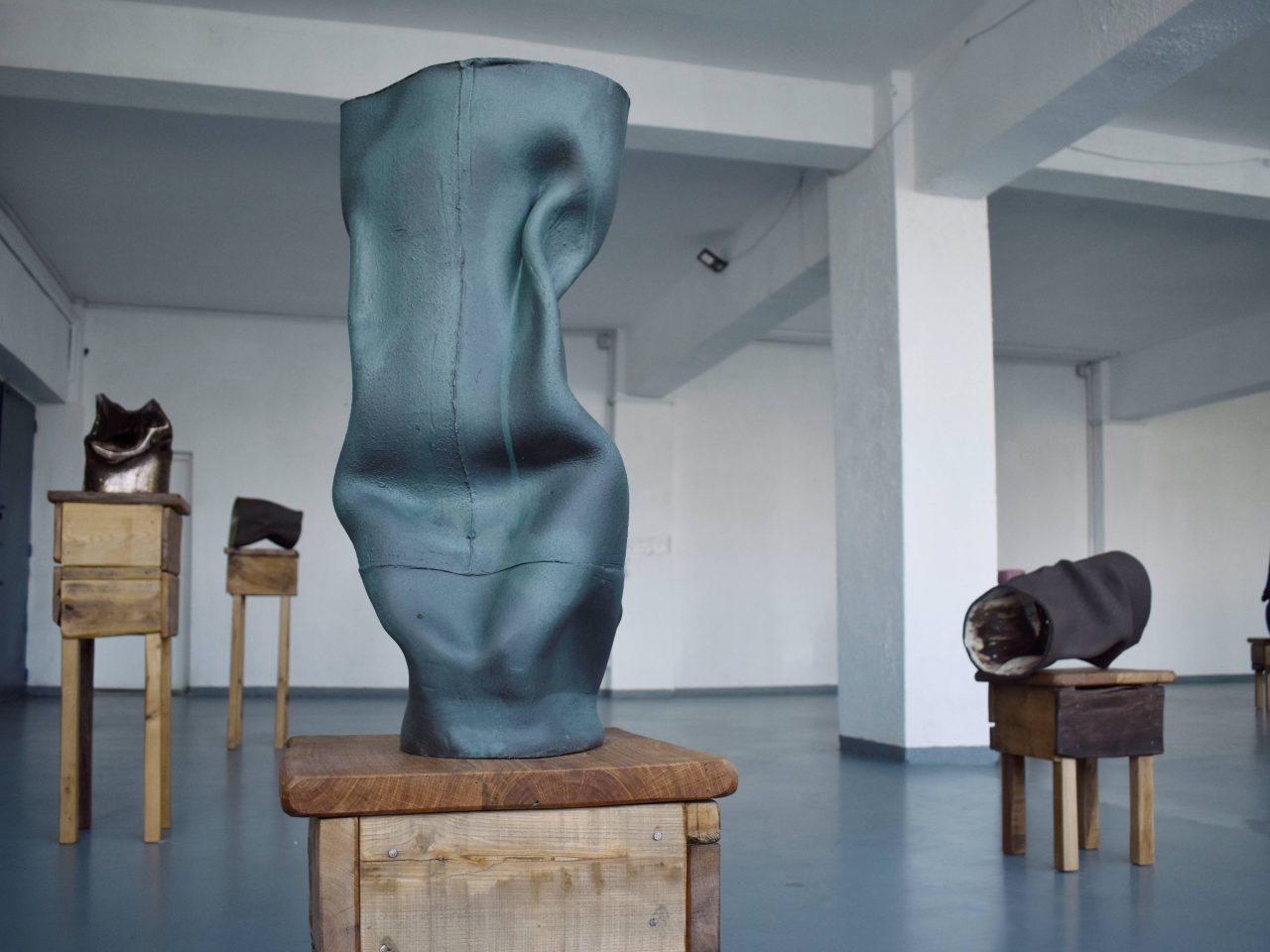 Clay vessels. All placed on small wooden tables, the shape of them are imprinted with the artist's embrace before it was dry, making them look crumpled.